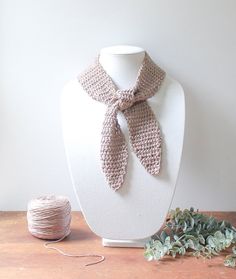 a crocheted scarf sits on a mannequin next to a ball of yarn