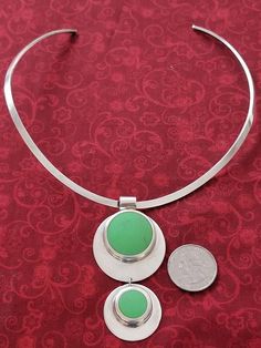 Sterling silver choker collar necklace with a large pendant.  The pendant consists of two silver discs with the smaller one hanging from the larger one.  Each silver disc has a large green stone that is off center.  It is a heavy piece of jewelry.  It is a beautiful, unusual necklace. Green Necklace With Coin Pendant, Green Coin Pendant Jewelry, Green Coin Pendant Medallion Jewelry, Modern Green Round Pendant Jewelry, Green Medallion Pendant Jewelry, Modern Green Circular Jewelry, Green Medallion Jewelry With Large Pendant, Modern Green Necklace With Round Pendant, Green Medallion Sterling Silver Jewelry