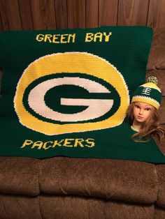 a green bay packers pillow with a doll wearing a knitted hat sitting on top of it