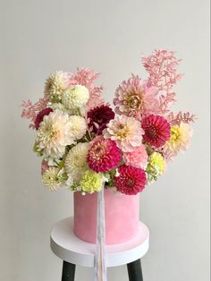 a pink and white cake with flowers in it on a small table next to a stool