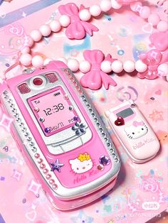 a pink hello kitty cell phone next to two smaller phones on a table with beads