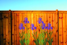 purple flowers painted on the side of a wooden fence with green grass in front of it