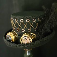 This striking top hat with embellished goggles and chain feature will quickly become your favorite hat! 100% wool felt, fully lined, fine apparel quality 5" tall crown with 2.5" curled brim in the Victorian style The top of the hat features a grommet and chain detail that wraps around the entire hat and is very eye catching. Bronze color goggles are embellished with gears and a large compass Three long feathers at the side add additional detail Black gimp trims the brim of the hat as well as the Steampunk Top Hat With High Crown For Themed Events, Vintage Top Hat With Short Brim For Themed Events, Steampunk Top Hat With Curved Brim For Costume, Vintage Ceremonial Costume Hat With High Crown, Vintage High Crown Top Hat For Costume Party, Vintage Top Hat For Costume Party, Adjustable High Crown Top Hat For Themed Events, Fitted Brimmed Hat For Themed Events, Steampunk Fitted Top Hat For Themed Events