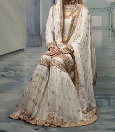 a woman in a white and gold bridal gown sitting on the floor with her hand on her hip