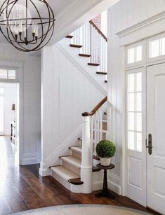 a foyer with white walls and wooden floors, chandelier over the stairs and door leading to another room