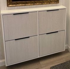 a white cabinet with two drawers and a painting on the wall in front of it