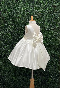 Our enchanting Knee Length flower girl dresses are sure to turn heads! This beautiful elegant sophisticated dress is handmade, the bodice consists of Ivory Bridal Satin followed by a flower belt (NOT DETACHABLE) the back of the dress consists of an open V-back with a zipper. The big bow is detachable. The skirt consists of Ivory  satin followed by lining and crinoline for a fuller look. Extremely light weight and beautiful. This dress is perfect for any occasion!  Dress Is Pictured with a pettic Elegant Spring Princess Dress For Baptism, Elegant Sleeveless Pageant Dress For Spring, Elegant Sleeveless Spring Pageant Dress, Elegant Spring Baptism Dress, Cream Wedding Dress With Bow, Elegant First Communion Dress For Spring, Cream Sleeveless Princess Dress For First Communion, Elegant Spring First Communion Dress, Princess Dress With Satin Bow For Baptism