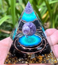 a hand holding a glass pyramid with blue and purple items in it's center