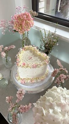 there is a white cake with pink flowers on the table next to other cakes and vases