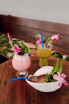 two cocktails are sitting on a table with strawberries and flowers in the cups