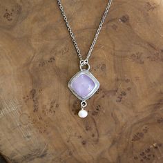 New! Purple Chalcedony Dyna Necklace. Gorgeous and unique Soft, Cool Violet Purple Chalcedony Cushion Square Cabochon is set tipped like a diamond in.925 Sterling Silver - paired with a lustrous, freshwater pearl dangle. All .925 Sterling Silver - includes .925 Sterling Silver chain. We've tipped the square like a diamond for dynamism, and to feature the stone in this new LBJ original. Dyna Necklace in Purple Chalcedony. With a minimal .925 Sterling Silver setting - this Purple Chalcedony Quartz Silver Jewelry With Square Pearl Pendant, Sterling Silver Pendant Necklace With Bezel Setting, Anniversary White Gold Cabochon Necklace, Sterling Silver Pendant With Bezel Setting, Sterling Silver Pendant Jewelry With Bezel Setting, Sterling Silver Cabochon Necklace Fine Jewelry, Sterling Silver Cabochon Necklace In Fine Jewelry Style, Sterling Silver Cabochon Necklace For Anniversary, One Of A Kind Sterling Silver Necklace For Anniversary