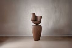 a tall wooden vase sitting on top of a hard wood floor next to a wall