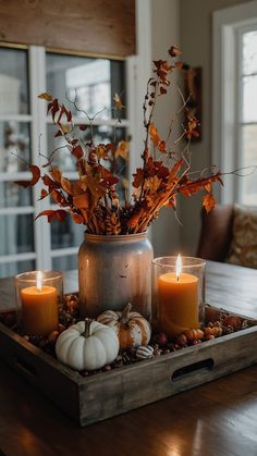 candles are lit on a tray with autumn leaves and pumpkins in the centerpiece