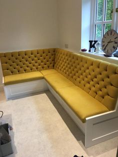 a yellow couch sitting in front of a window next to a white table with a clock on it