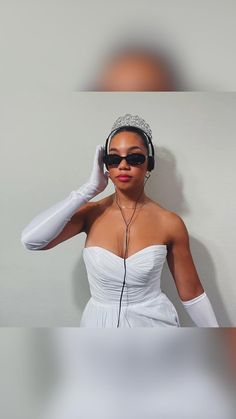 a woman in white dress wearing headphones and holding her hands to her ears while standing next to a wall