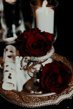 two red roses sitting on top of a silver plate next to a candle and napkin