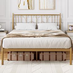 a bed with white linens and gold headboard in a large room, next to two pictures on the wall