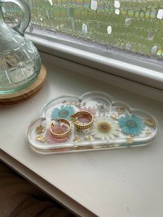 two wedding rings are sitting on a tray next to a vase and window sill