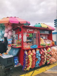 a candy stand with umbrellas and balloons on the side of the road in front of it