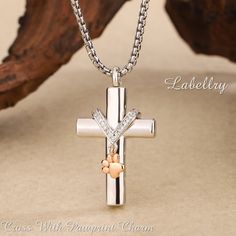 1. Serene Holy Cross Pendant: Our Cremation Necklace With Pawprint Charm features a sterling silver cross pendant of stunning elegance, crafted meticulously to honor your cherished pet's memory. This graceful design embodies sacred symbolism and is a treasured keepsake for pet lovers. Inspired by the enchanting bond we share with our beloved pets, the Memorial Necklace with Enchanted Pawprints is a sacred emblem of remembrance and affection, providing comfort during the grieving process. 2. Gold Personalized White Cross Necklace, Elegant Memorial Cross Jewelry, Elegant Cross Pendant Jewelry For Memorial, Elegant Cross Jewelry For Memorial, Engraved White Gold Cross Necklace As Gift, Engraved White Gold Cross Necklace Gift, Personalized White Gold Cross Pendant, Silver Cross Necklace For Mother's Day, Silver Cross Pendant Necklace For Mother's Day