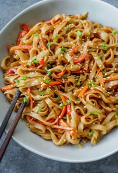 a white bowl filled with noodles, carrots and green onions next to chopsticks