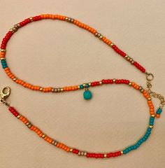 an orange and blue beaded necklace on a white surface with a gold charm hanging from it's end