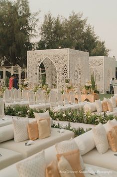 rows of white couches covered in pillows and greenery at an outdoor wedding reception