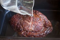 someone is pouring water on an uncooked piece of meat in a pan with other food items