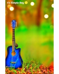 a blue guitar sitting on the ground in front of some grass and trees with boke lights behind it