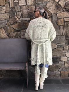 a woman standing in front of a stone wall next to a gray bench and chair