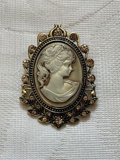 "This beautiful CAMEO brooch/pin is very attractive in its Victorian design. The face is 1.5\" and so pretty. The lenth is 2.5\". Her hair is in an upsweep with tendrils.  The perimeter of the brooch is filled with topaz-like crystals.  The cameo is made from a resin product. It is very attractive on a suit, blouse, scarf or dress. Can also be used as a wedding lapel pin. This brooch is available for immediate shipment via USPS First Class Mail. At an additional cost, this can be sent via Priori Blouse Scarf, Wedding Lapel, Lapel Pins Wedding, Long Beach Ny, Suit Blouse, Resin Product, Scarf Pin, Topaz Color, Victorian Design