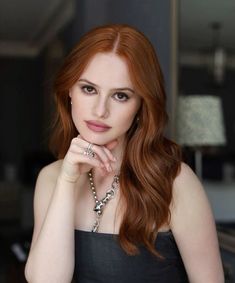 a woman with red hair wearing a black dress and holding her hand on her chin