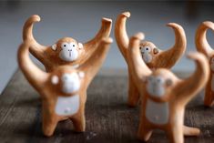 three ceramic monkey figurines standing on top of a wooden table with their arms in the air