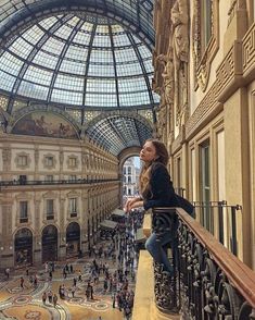 a woman standing on top of a balcony next to a glass ceiling filled with people