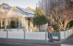 a man standing in front of a white picket fence next to a tree and house