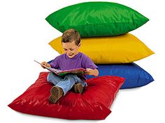 a young boy sitting on top of a pile of pillows while looking at a book