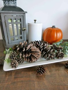 pine cones and greenery sit on a white tray next to a candle holder, pumpkins and candlesticks