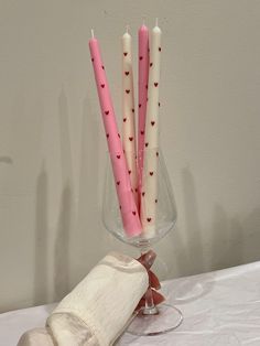 pink and white candles are in a glass vase on a table with a napkin next to it