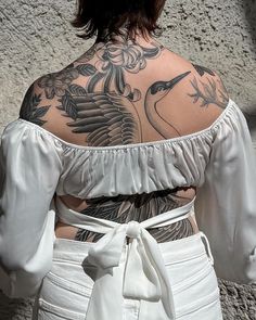 the back of a woman's white top with tattoos on her arms and shoulder