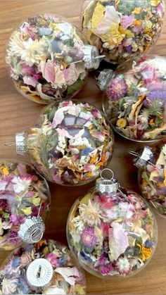 several glass ornaments with flowers in them sitting on a wooden table next to each other