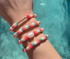 a woman's arm with multicolored bracelets on top of it next to a pool