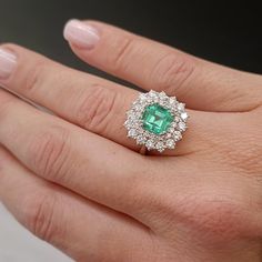 a close up of a person's hand wearing a ring with an emerald and diamond center