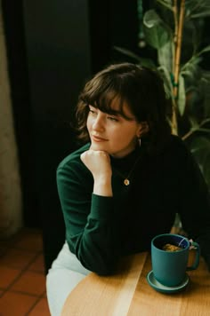 a woman sitting at a table with a cup of coffee in front of her and looking off to the side