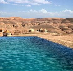 a body of water in front of some hills and sand dunes with huts on the other side