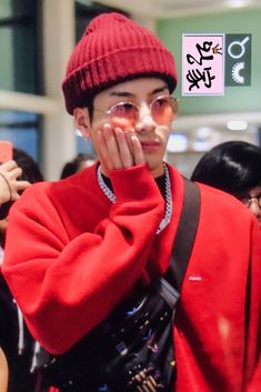 a young man wearing a red coat and hat holding his hand up to his face