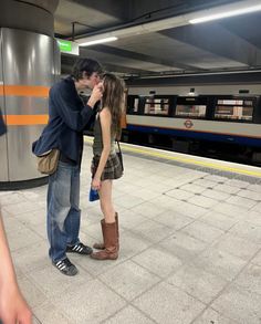 a man and woman standing next to each other in front of a train station platform