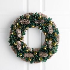 a wreath with pine cones and greenery hanging on a door