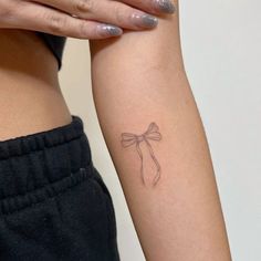 a woman's arm with a small bow tattoo on the left side of her arm