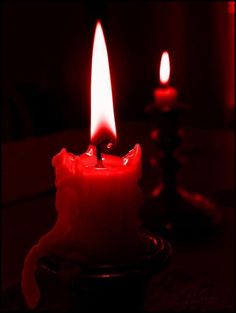 two lit candles sitting on top of a table in front of a red light behind them