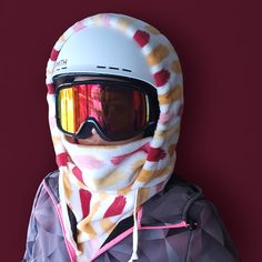 a person wearing ski goggles and a scarf around their neck, standing in front of a red background